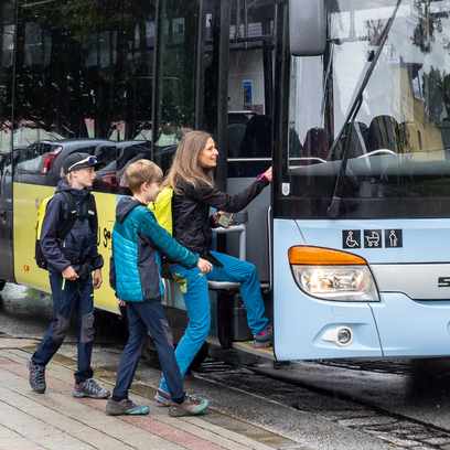 Mutter mit zwei Kindern, die in einen Bus einsteigen.